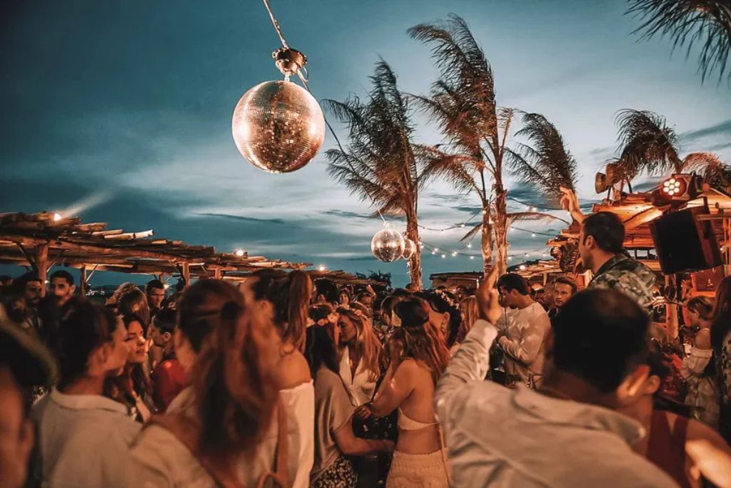 Guests enjoying a sunset party at an exclusive beach club in Mykonos, Greece.