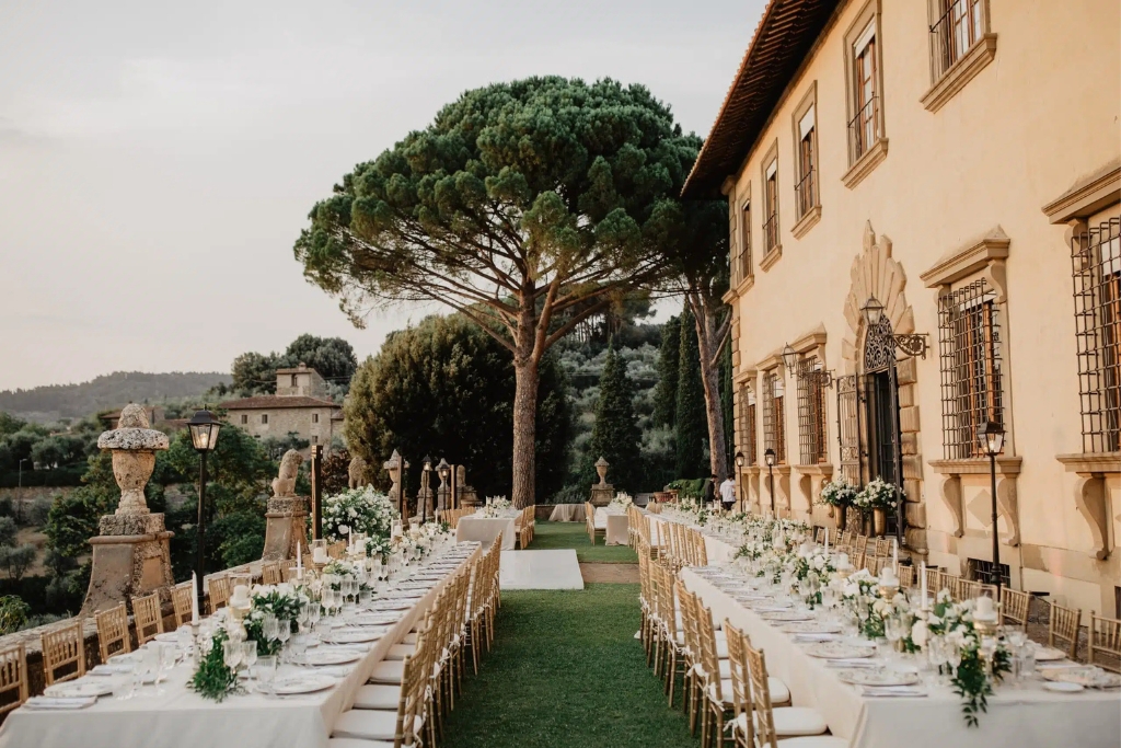 Elegant outdoor summer wedding reception with long dining tables set in the gardens of a countryside villa.