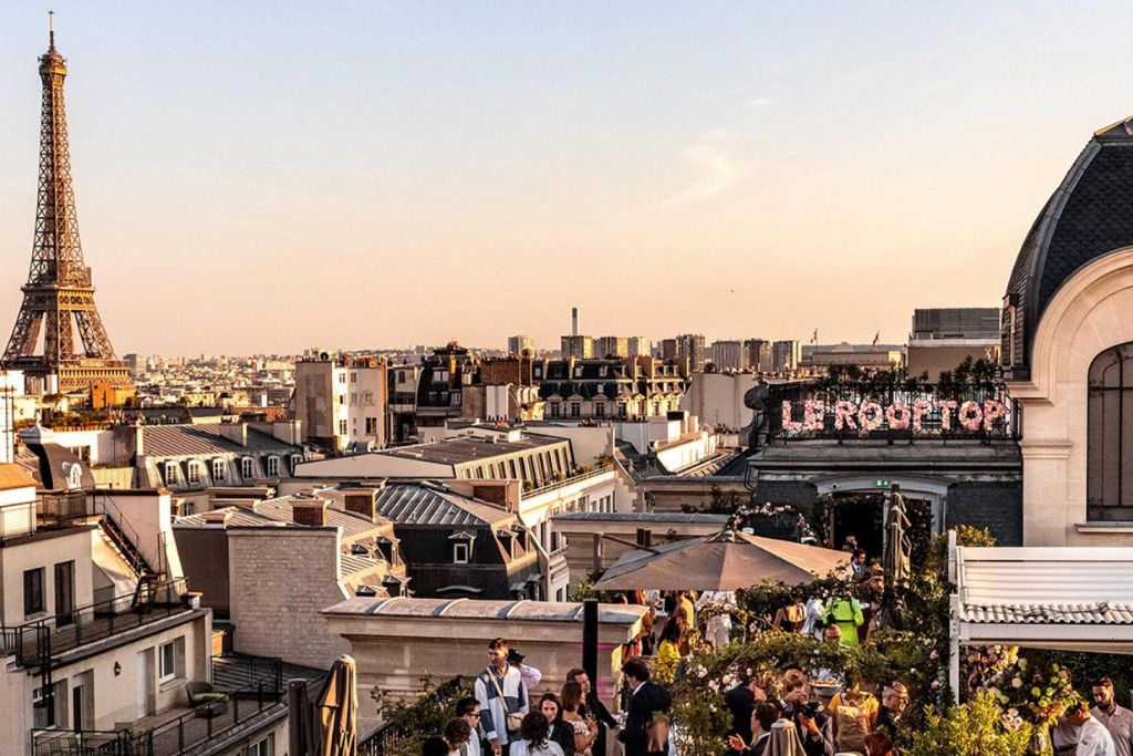 Guests enjoying a rooftop party overlooking the Paris skyline and the Eiffel Tower at sunset.