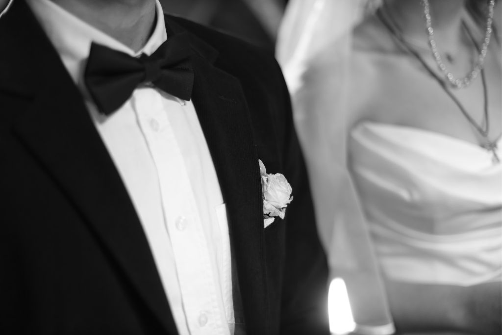 Close-up of a groom in a black tuxedo and bow tie beside his partner at an elegant black tie wedding.