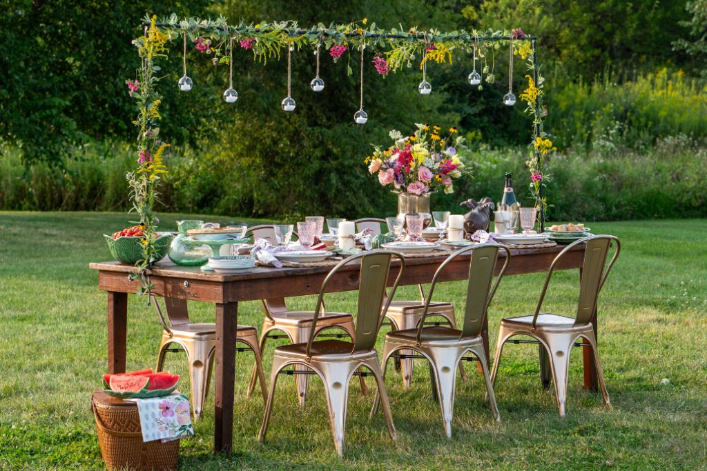 Outdoor garden party table set on a lawn with flowers, chairs and summer decorations in a green garden setting.