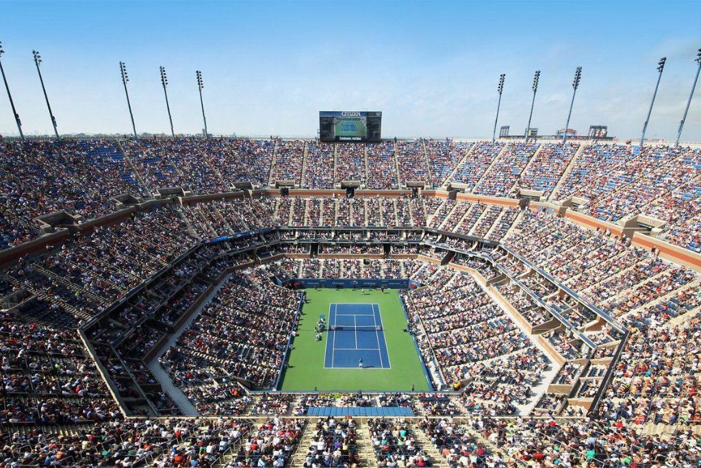 Crowded tennis stadium at the US Open with spectators watching a match on a bright summer day.
