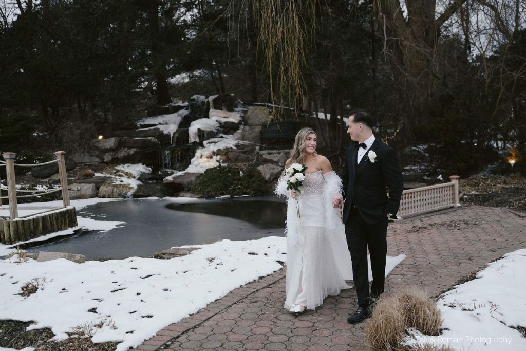 Bride and groom walking outdoors beside a snowy pond during a winter wedding celebration.
