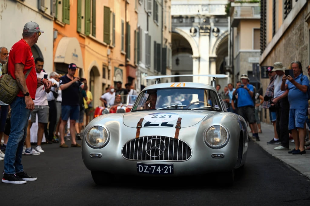 Classic Mercedes-Benz racing car driving through an Italian city street during the 1000 Miglia, surrounded by spectators.