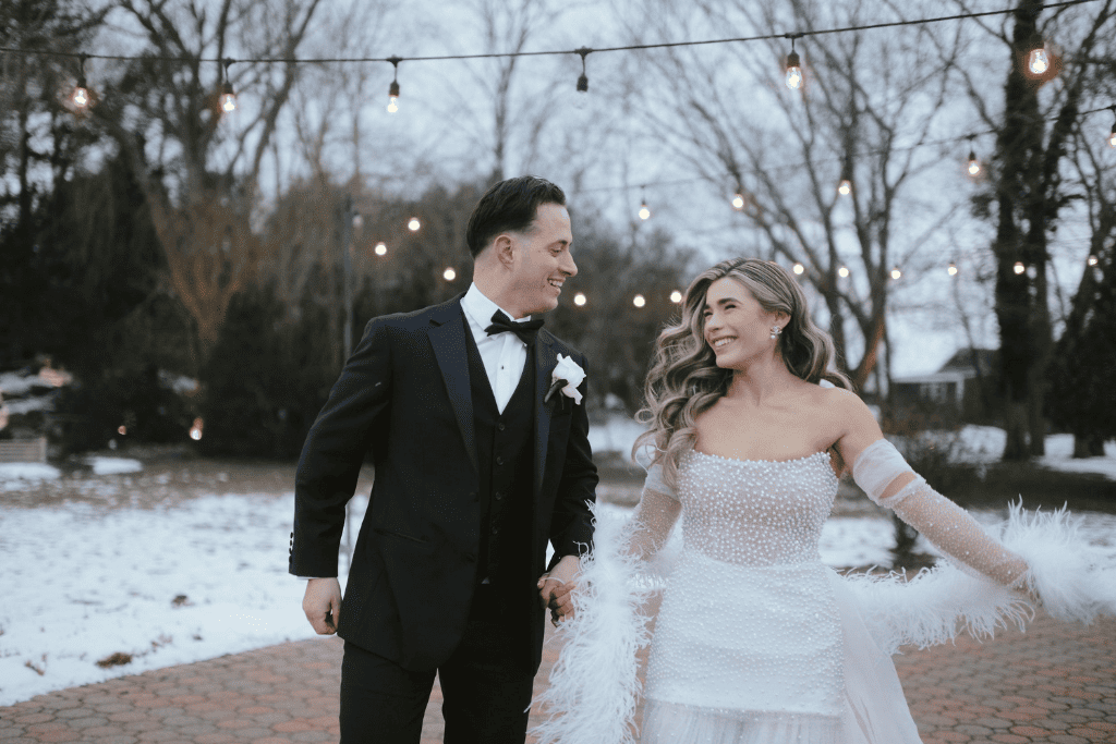 Bride and groom walking outdoors beside a snowy pond during a winter wedding celebration.