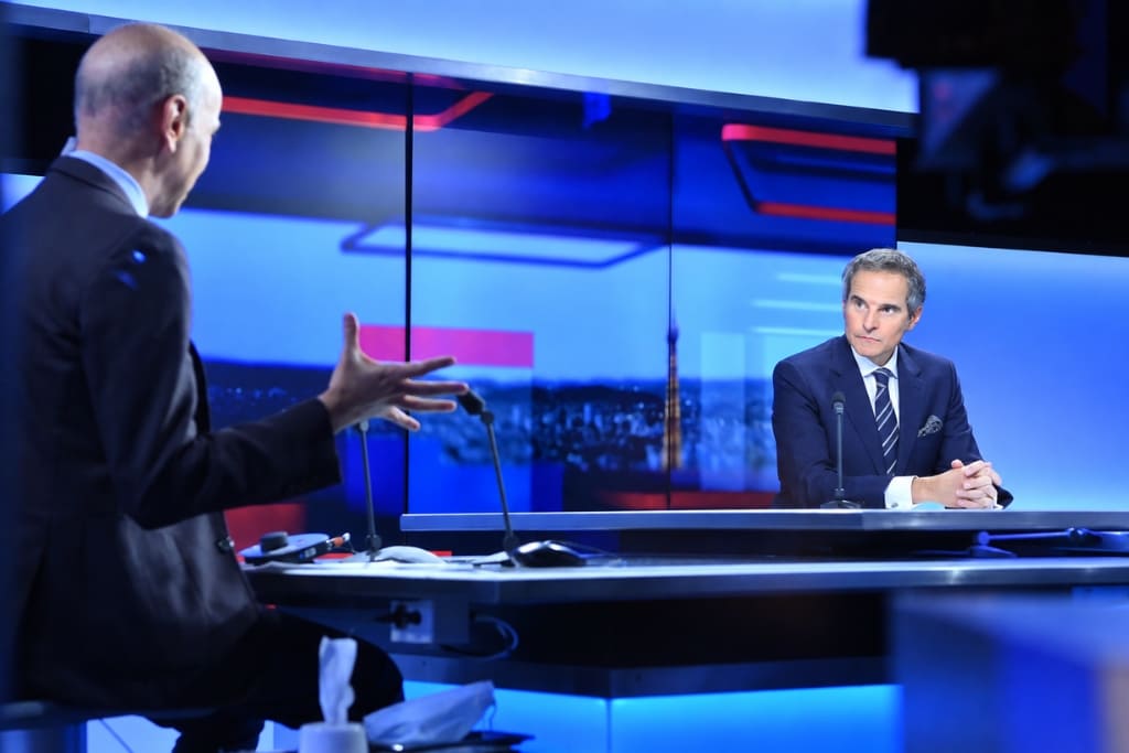 TV interview in a professional news studio, with a guest speaking to a presenter on camera.