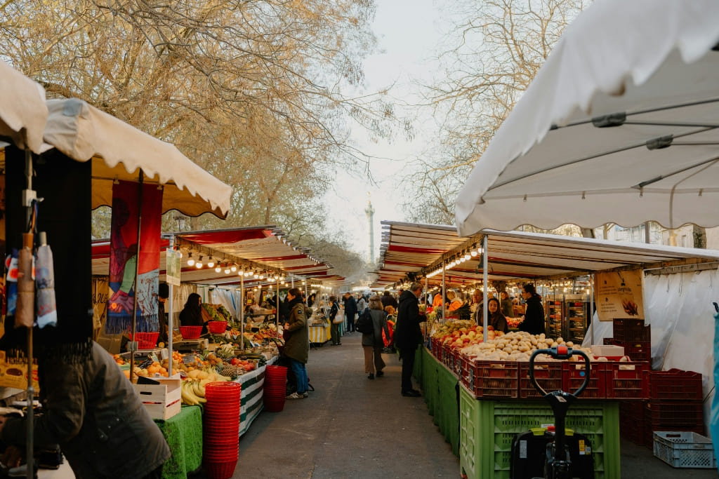 Shoppers browsing fresh produce stalls at an outdoor farmers market in Paris.