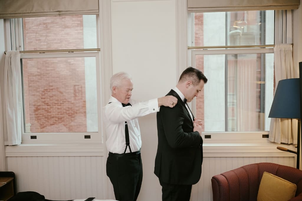 Man in a tuxedo getting ready for a black tie event, with another man adjusting his jacket.