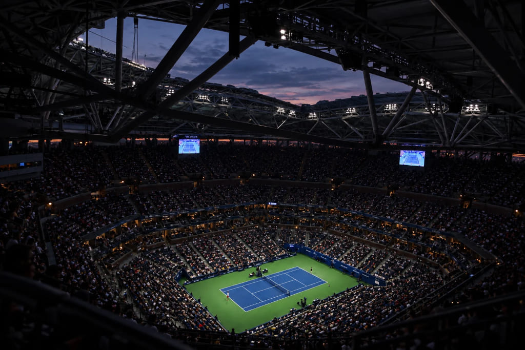 US Open tennis match at Arthur Ashe Stadium, with a packed crowd watching under the lights at night.