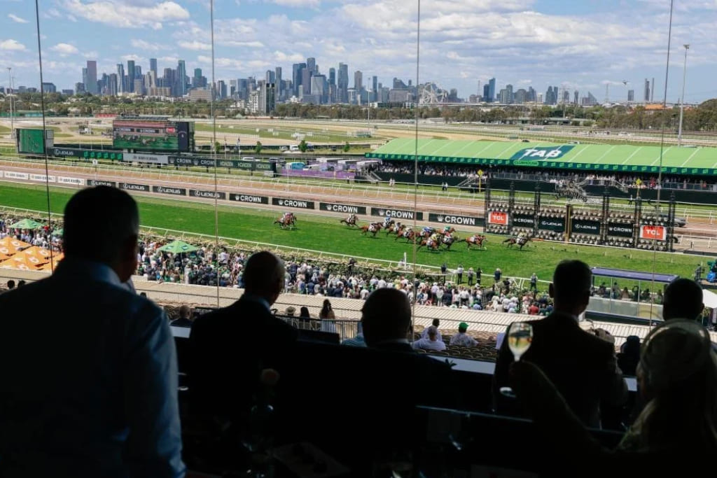 Horse racing at Flemington Racecourse during the Melbourne Cup, with spectators overlooking the track and Melbourne skyline in the background.