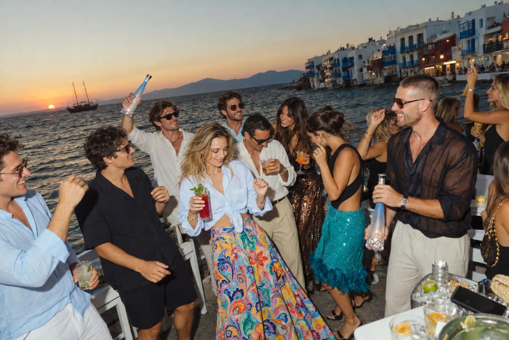 Guests dancing and enjoying drinks at a summer party by the sea in Mykonos at sunset.
