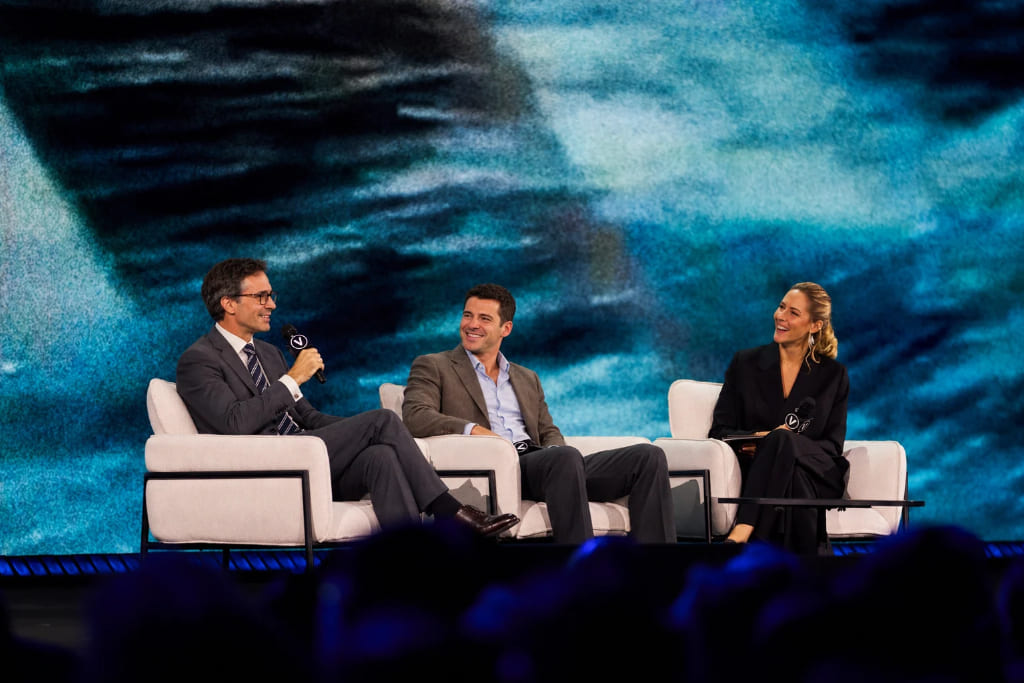 Business conference panel discussion with speakers on stage in front of a large audience.