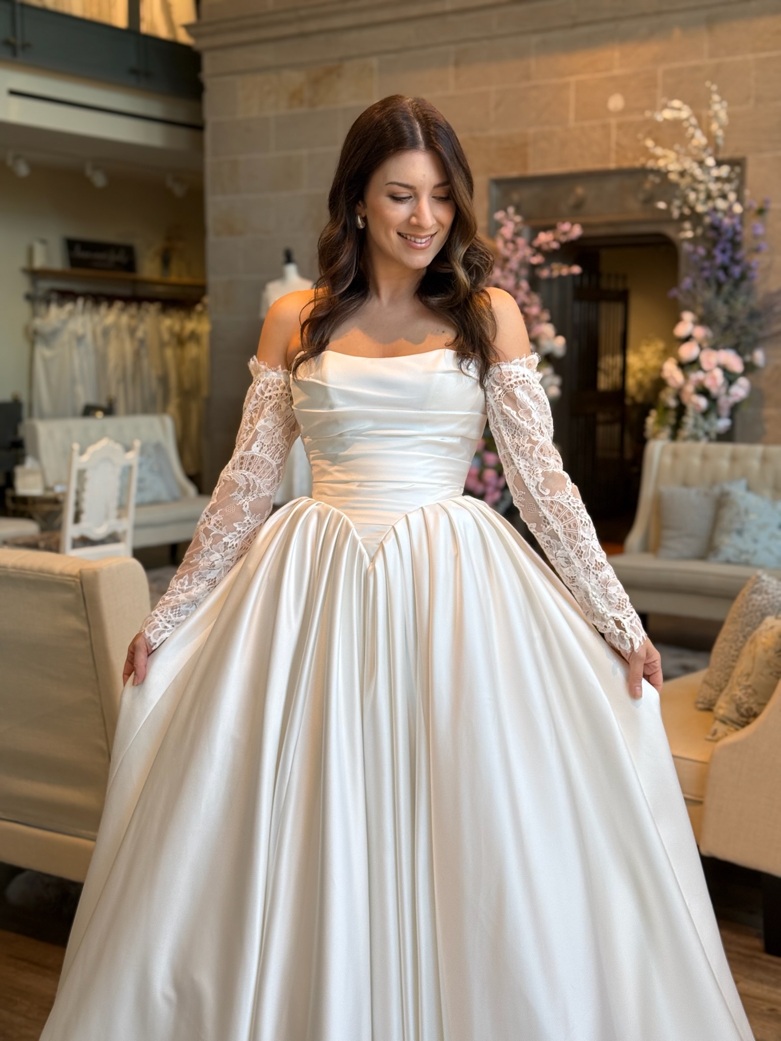 Bride wearing an elegant off the shoulder lace ball gown wedding dress in a luxury bridal boutique