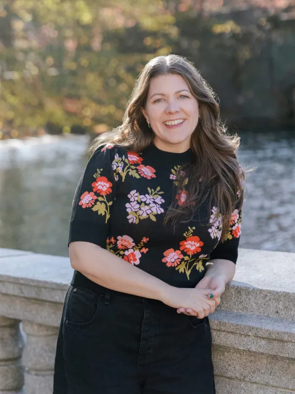 Jen Mayer, AFC® + founder of Fully Funded, wearing a black sweater with flowers, smiling.