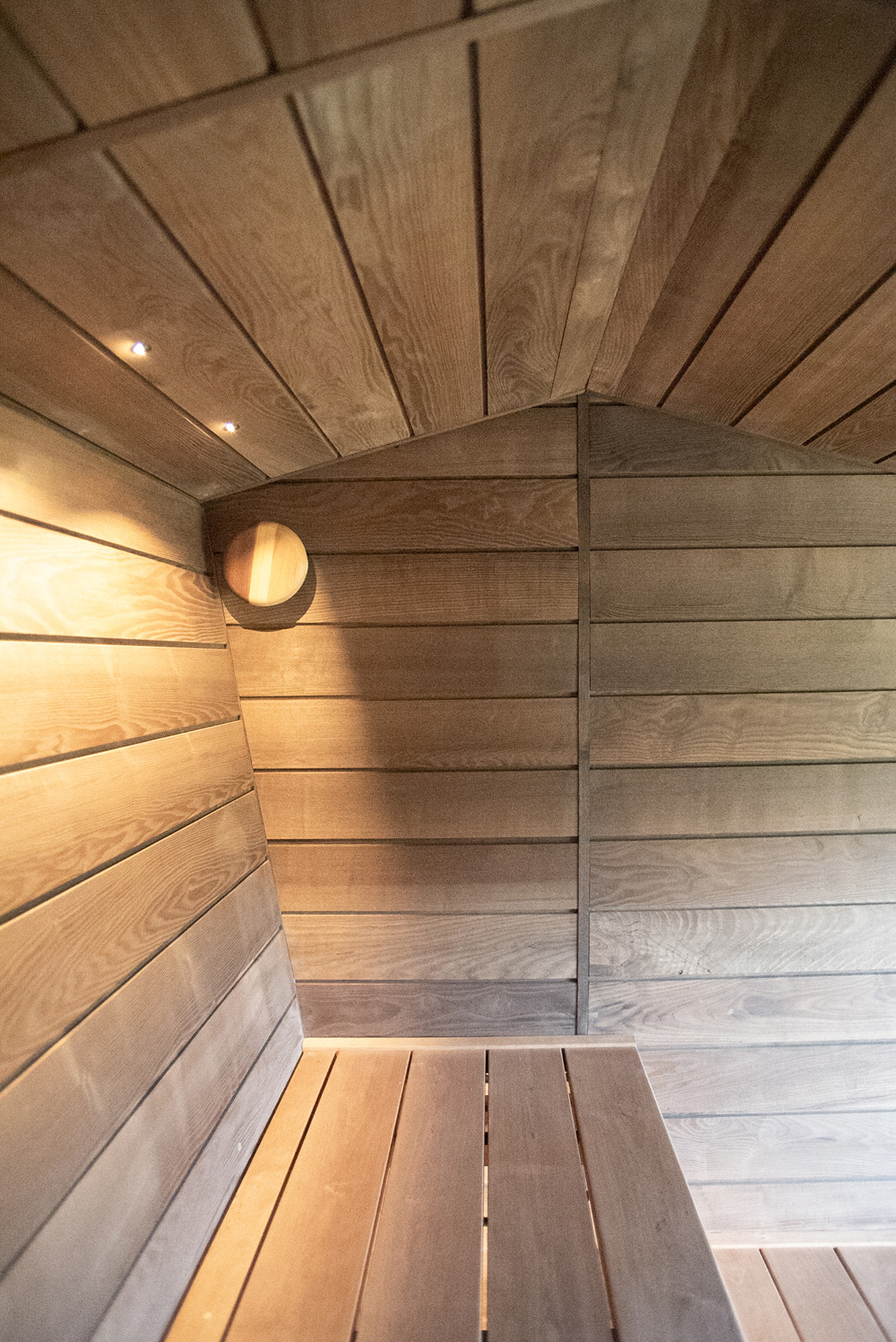 Interior of a wooden sauna featuring bench seating and soft lighting on paneled walls and ceiling.
