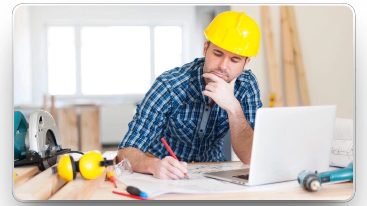 Construction worker sitting at a desk with blueprints, planning project maintenance.