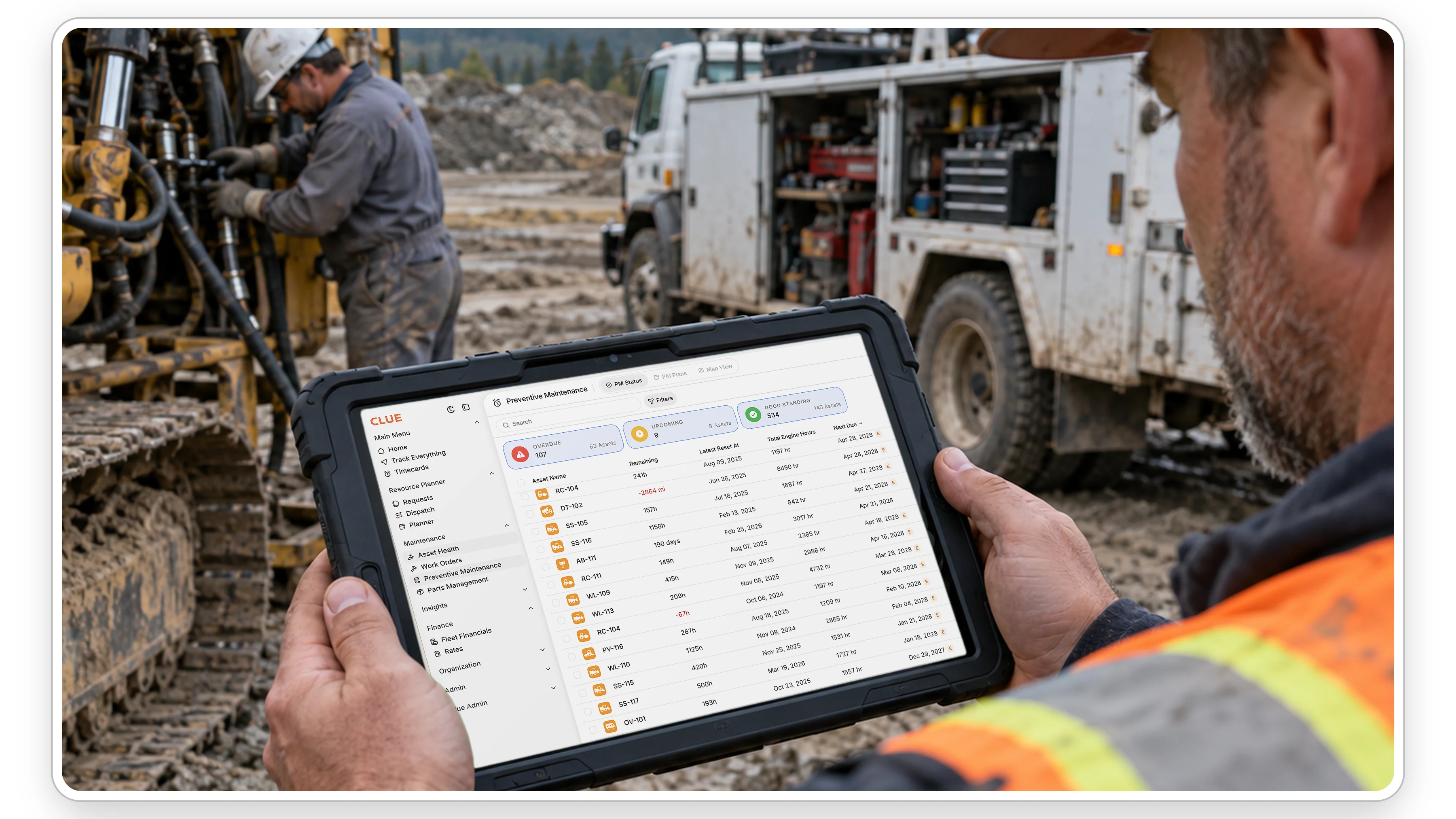 Shop foreman checking Clue preventive maintenance status on a tablet while a mechanic repairs an excavator