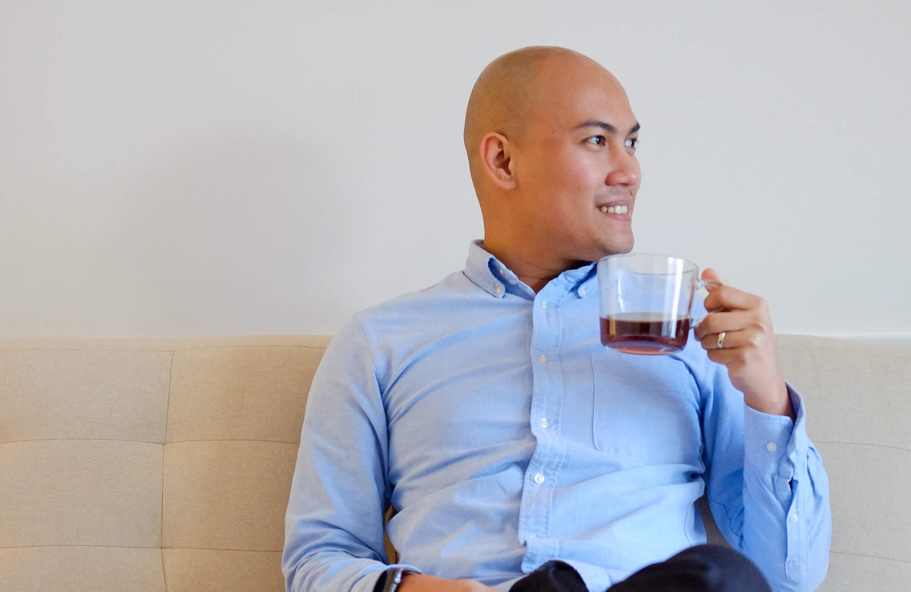 Photo of Eli smiling, holding a cup of coffee in one hand.
