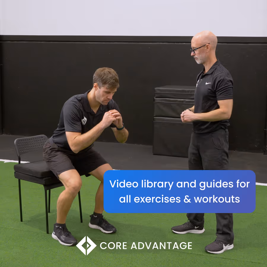 Fit man performing a squatting exercise sitting on a chair while being guided by a coach in a gym with green turf floor.