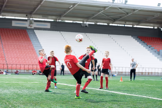 Young boys playing soccer indoors with one boy performing a high kick to control the ball.