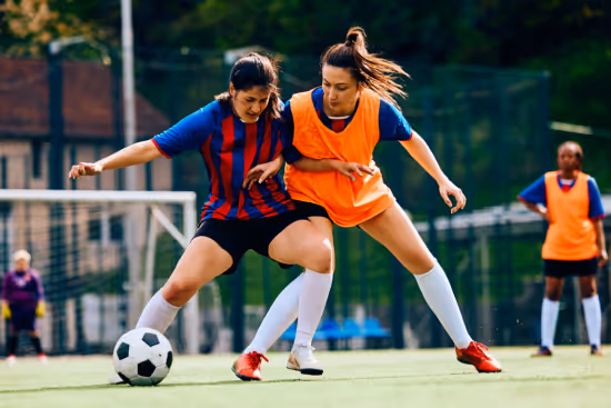 Two female soccer players competing for the ball on a grassy field during a match.