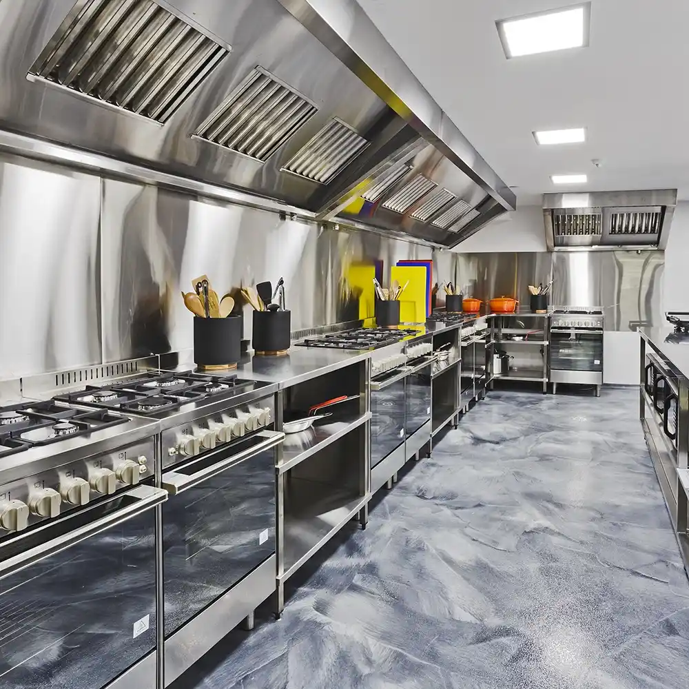 Modern commercial kitchen with stainless steel cooking equipment and slip-resistant epoxy flooring.