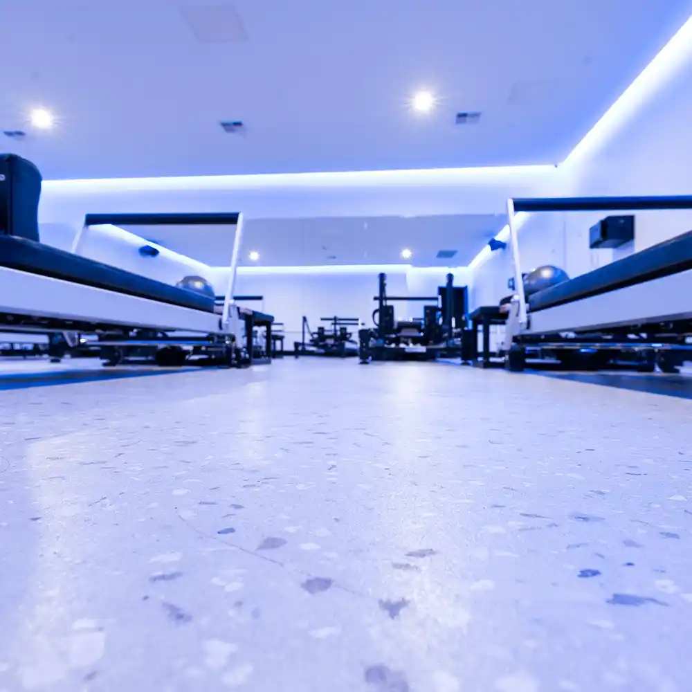 Polished concrete floor in a reformer Pilates studio, captured from ground level between exercise machines under bright LED lighting.