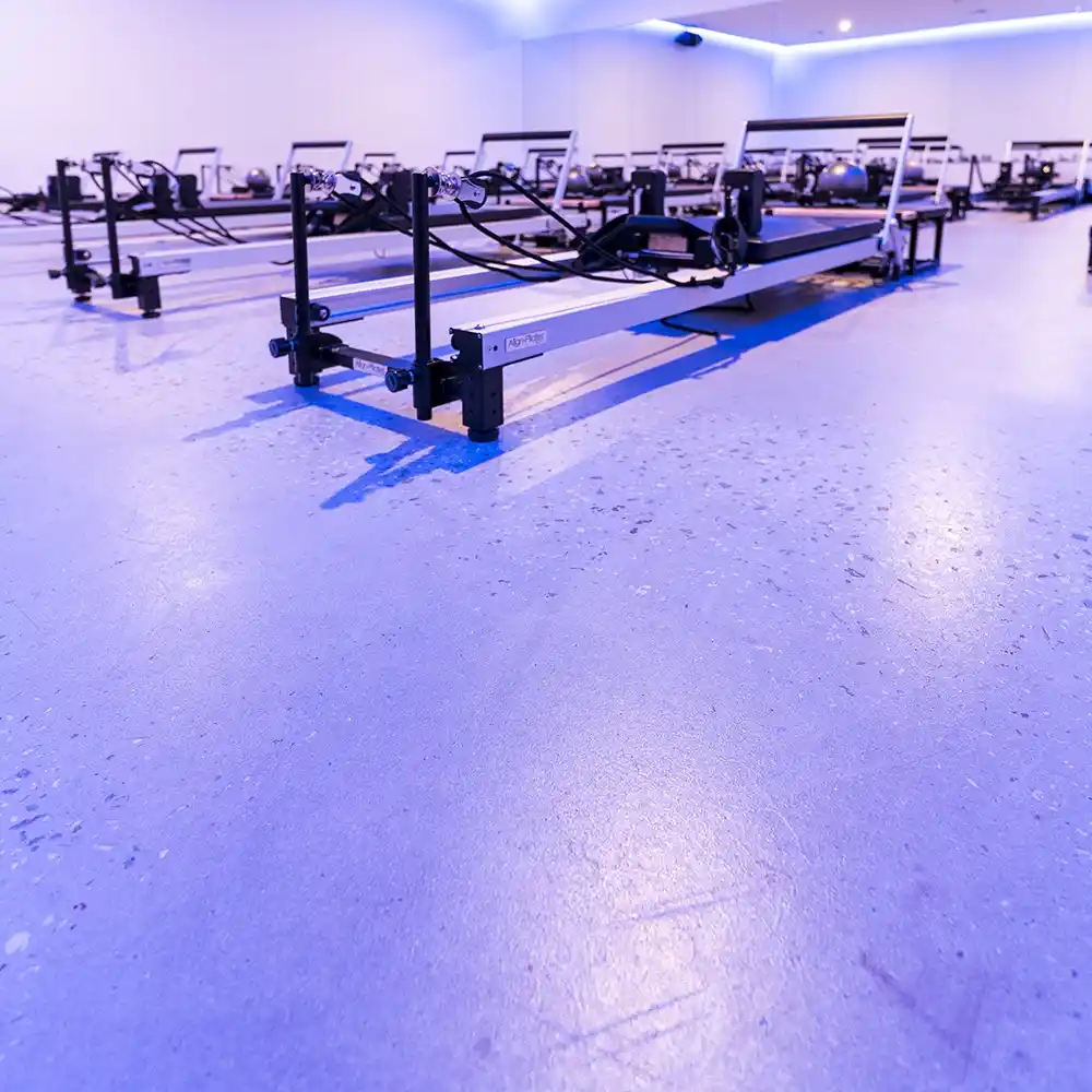 Wide shot of a reformer Pilates studio with seamless polished concrete flooring and blue-toned ambient lighting.