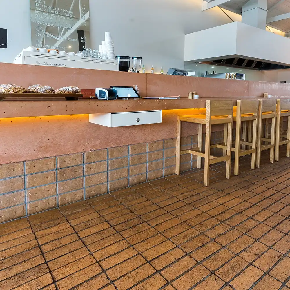 Terracotta-style tiled flooring in a contemporary cafe with a timber counter and wooden seating.