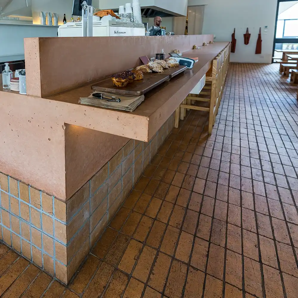 Spacious cafe interior featuring red tiled flooring, timber counters, and a chef behind the service area.