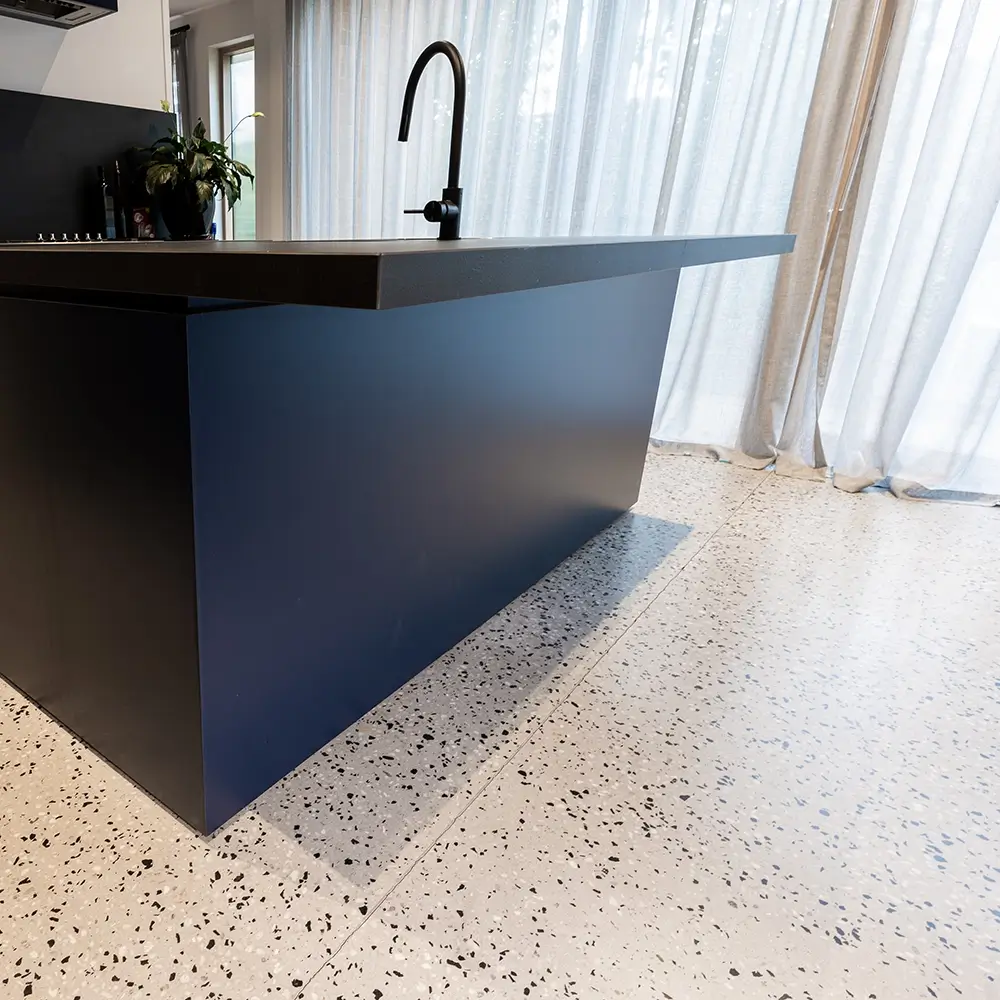 Modern commercial kitchen island with terrazzo-style epoxy flooring and sheer curtains in the background.