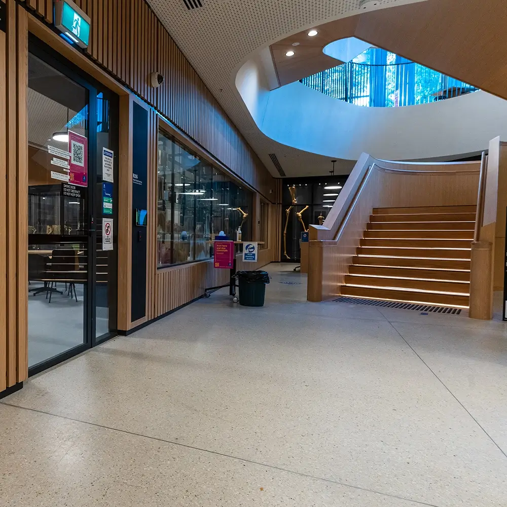 Non-slip concrete flooring in a school corridor with stairwell and glass windows.