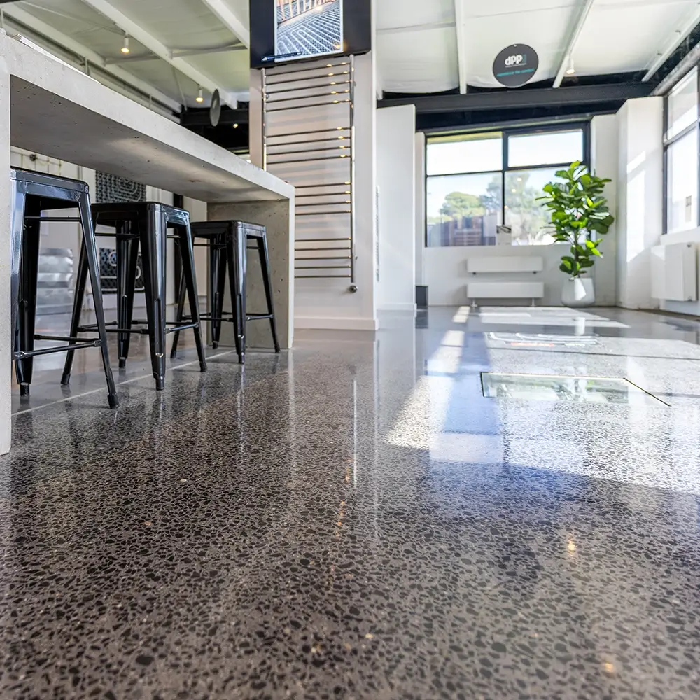Industrial-style polished concrete flooring under a concrete bench with stools in a bright showroom.]