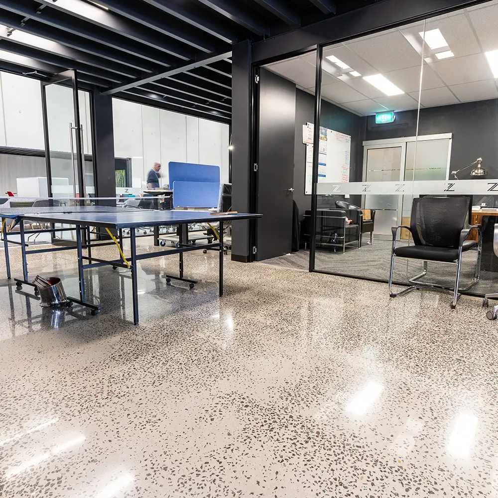 Polished concrete staircase landing with exposed brick feature wall and downlighting in a commercial building.