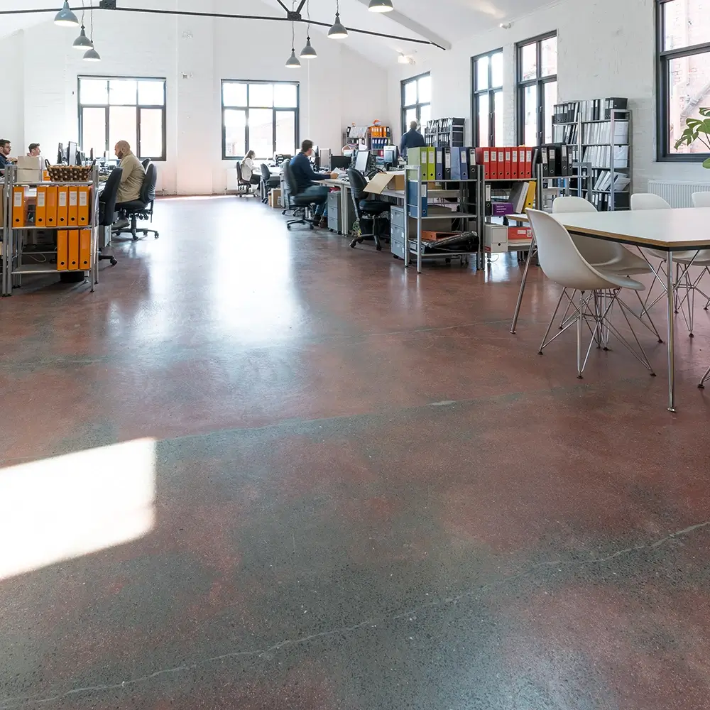 Large open-plan office with red-toned concrete flooring and industrial-style furniture.