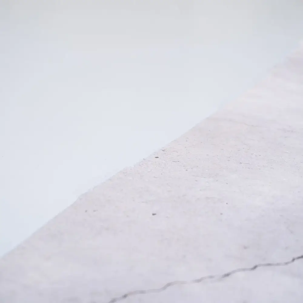Close-up view of a concrete floor transition, showing the difference between bare concrete with a visible crack and a freshly coated smooth epoxy surface.