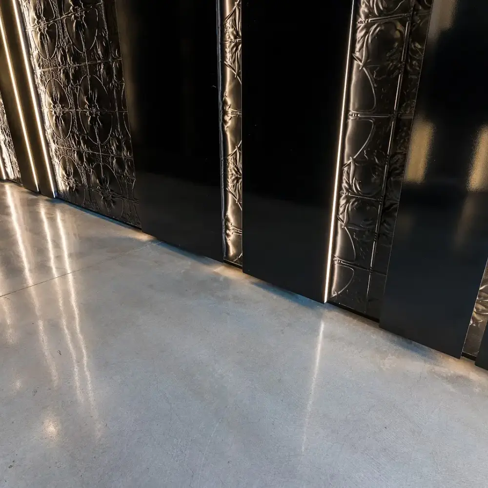 Shining concrete floor reflecting light from decorative black wall panels with vertical illuminated strips.