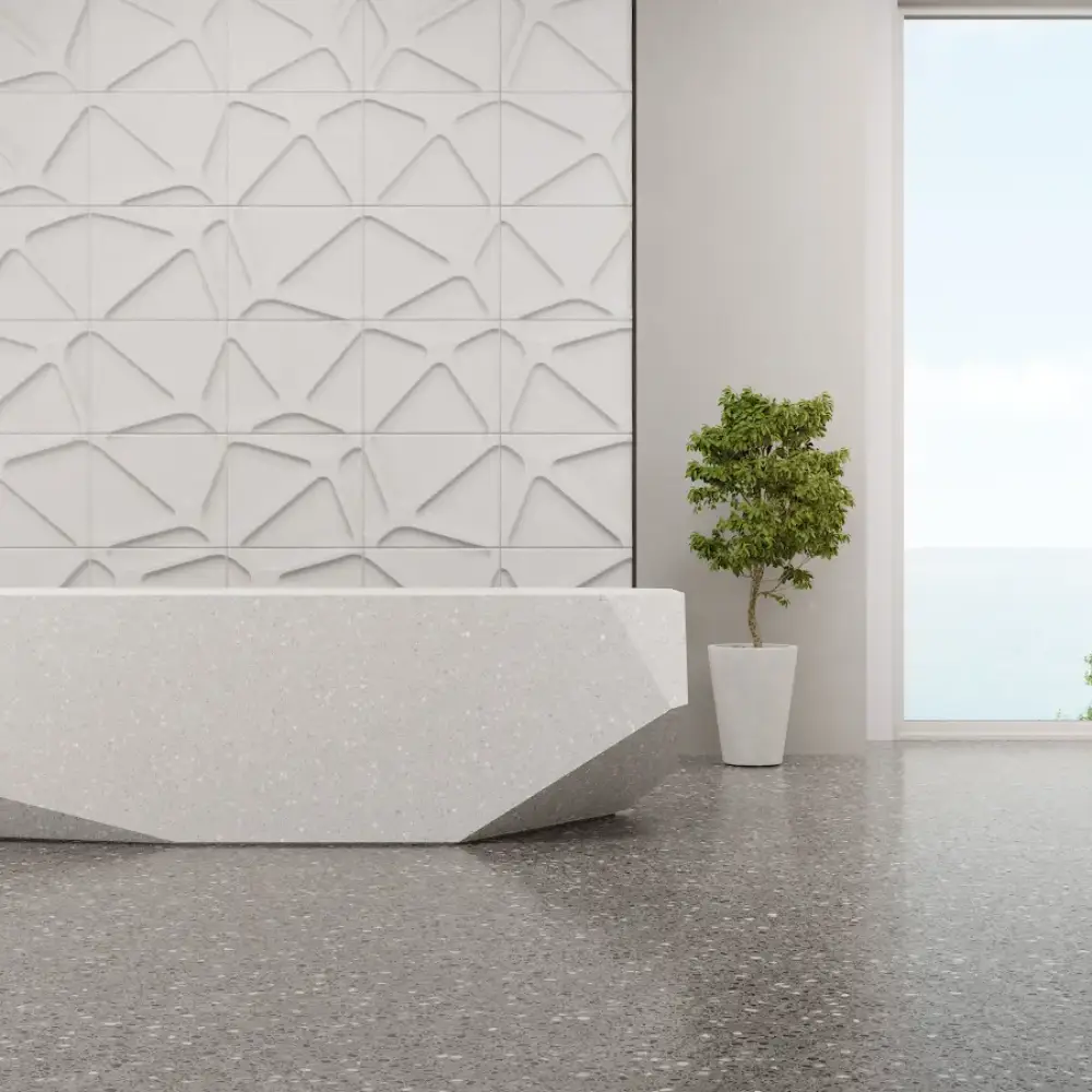 Modern minimalist interior with terrazzo flooring, a geometric white reception desk, textured feature wall, potted plant, and large window overlooking the ocean.