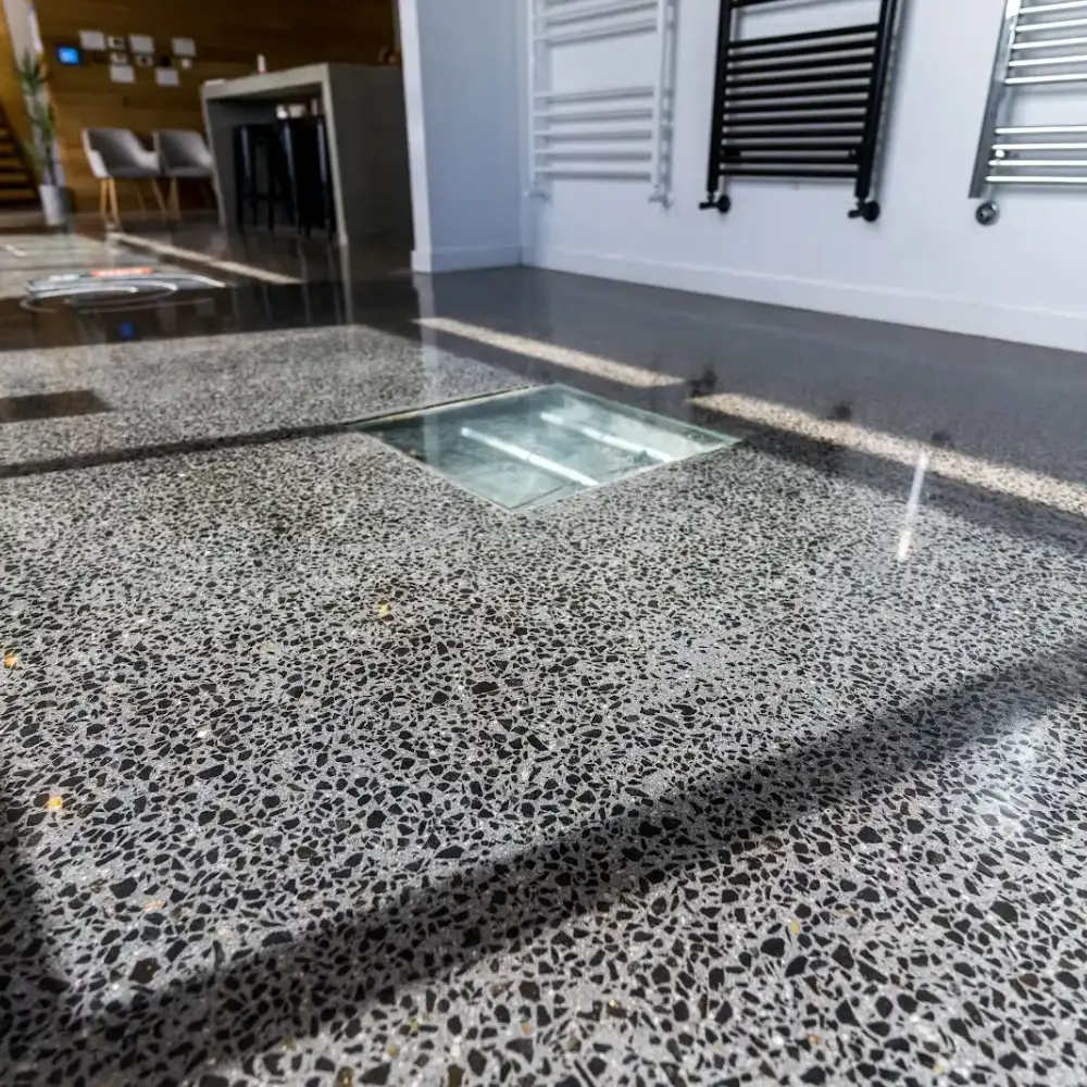 Polished terrazzo floor with a glass floor panel in a modern showroom featuring seating and wall-mounted fixtures.