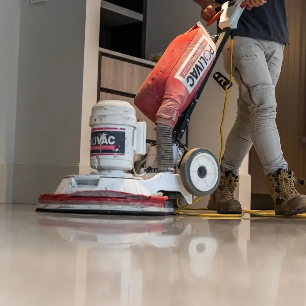 Close-up of a worker using a floor polishing machine on a smooth concrete surface indoors.