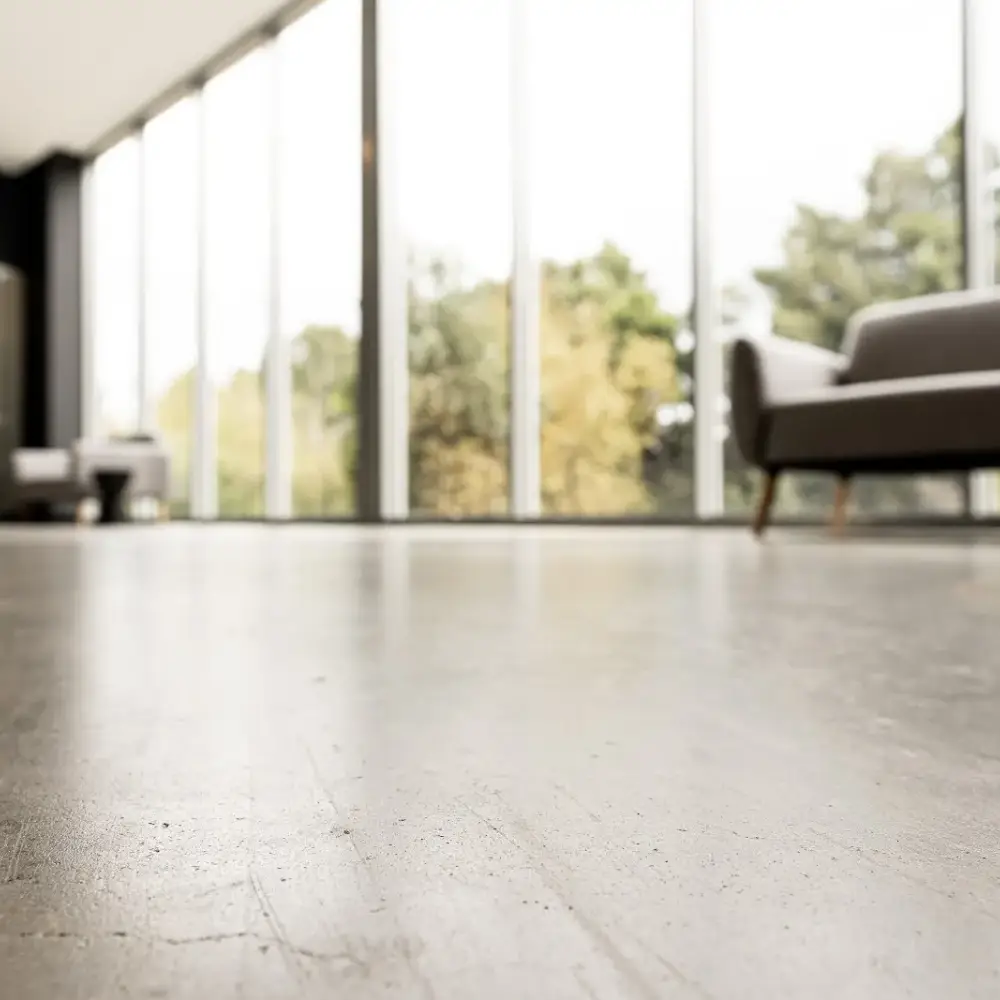 Close-up of a matte polished concrete floor in a modern room with large windows and minimal furniture.