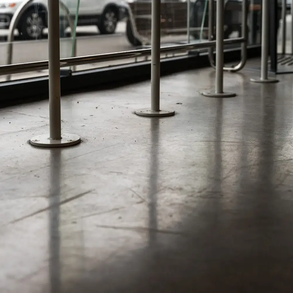 Matte polished concrete floor inside a storefront with white metal supports and street view through large windows.