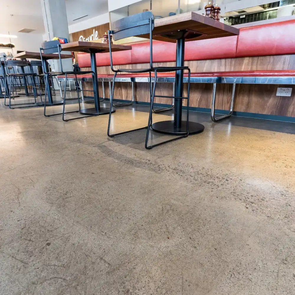 Polished concrete floor in a restaurant with wooden tables, black metal chairs, and red upholstered bench seating.