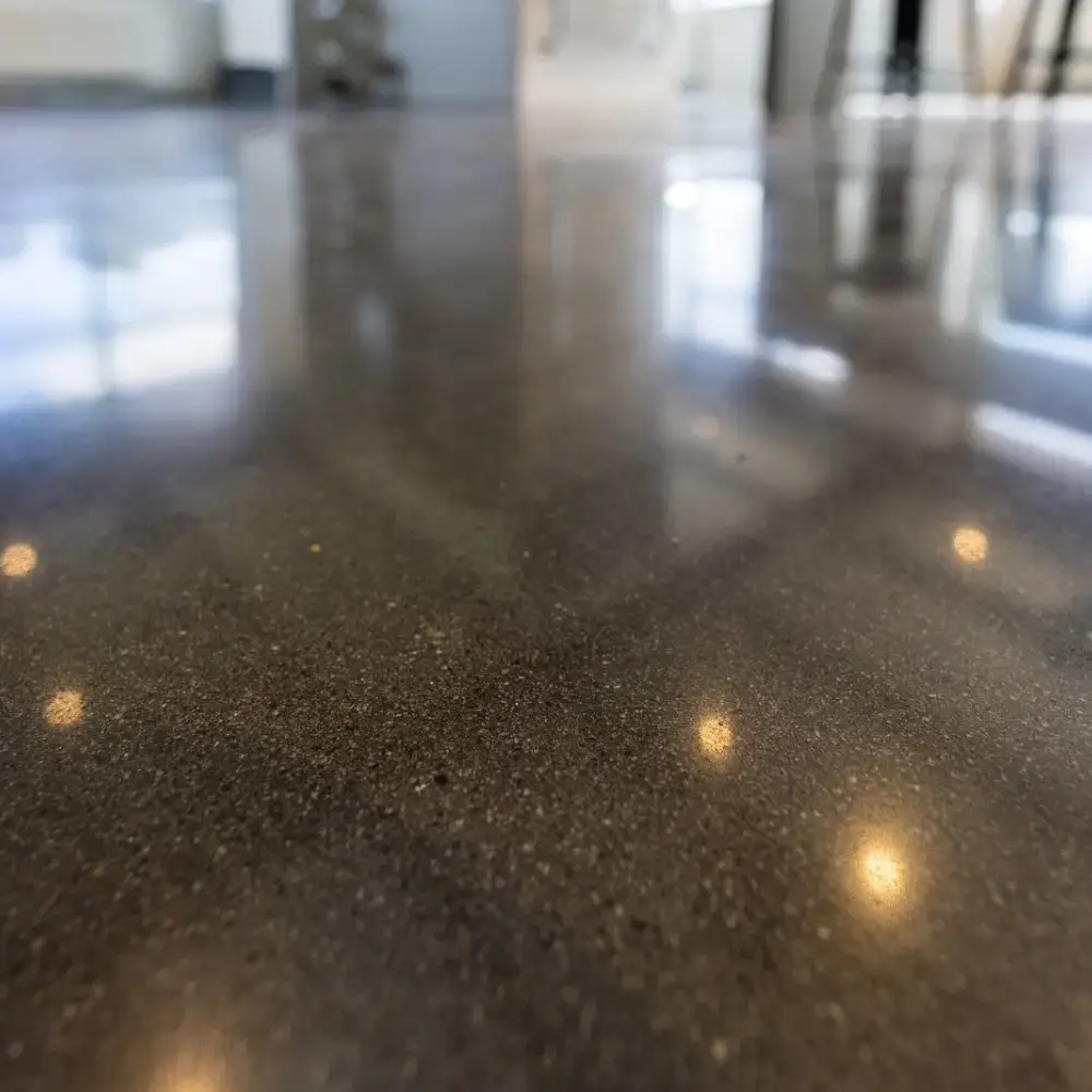 Close-up of a dark polished concrete floor with a glossy finish reflecting lights and windows.