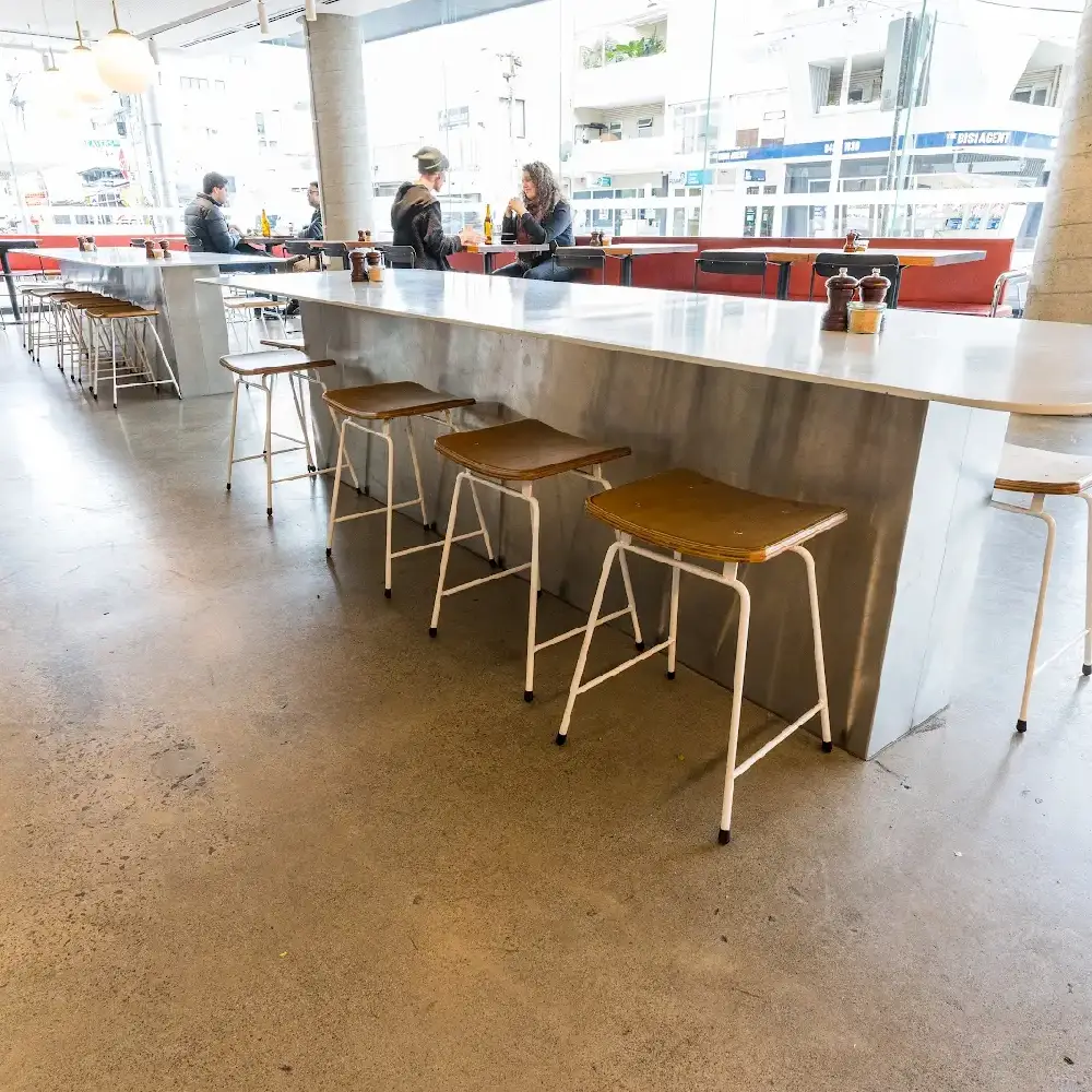 Modern café interior with polished concrete floor, high stools, and a long communal table.