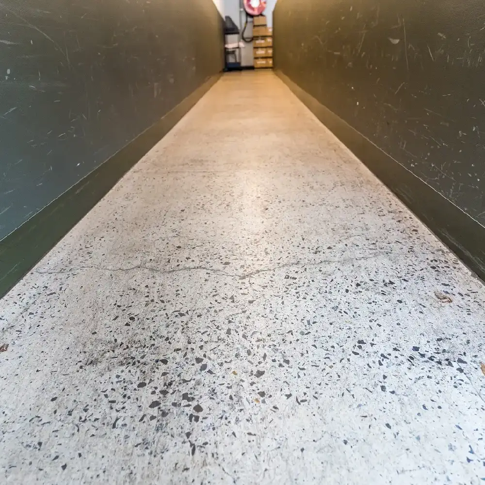 Narrow hallway with polished concrete floor and dark green walls marked by scratches.