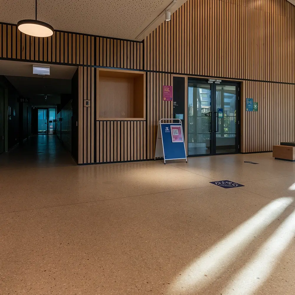 Polished concrete flooring in a university interior with timber wall panels and natural light.