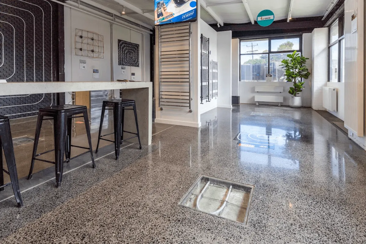 Modern showroom featuring high-gloss polished aggregate flooring, black bar stools, and underfloor heating displays.