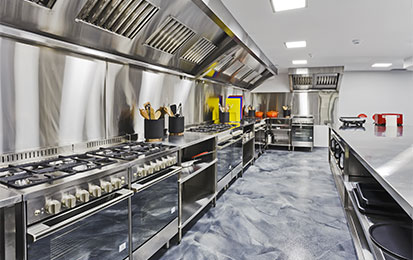 Commercial kitchen featuring stainless steel cooktops, rangehoods, and durable grey metallic commercial flooring.