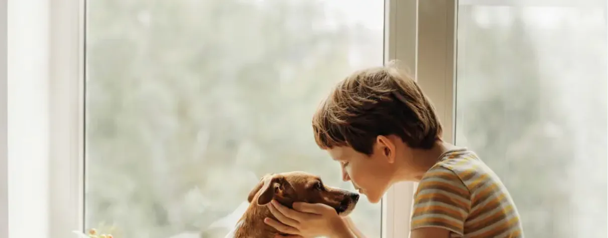 Child hugging a dog by a window